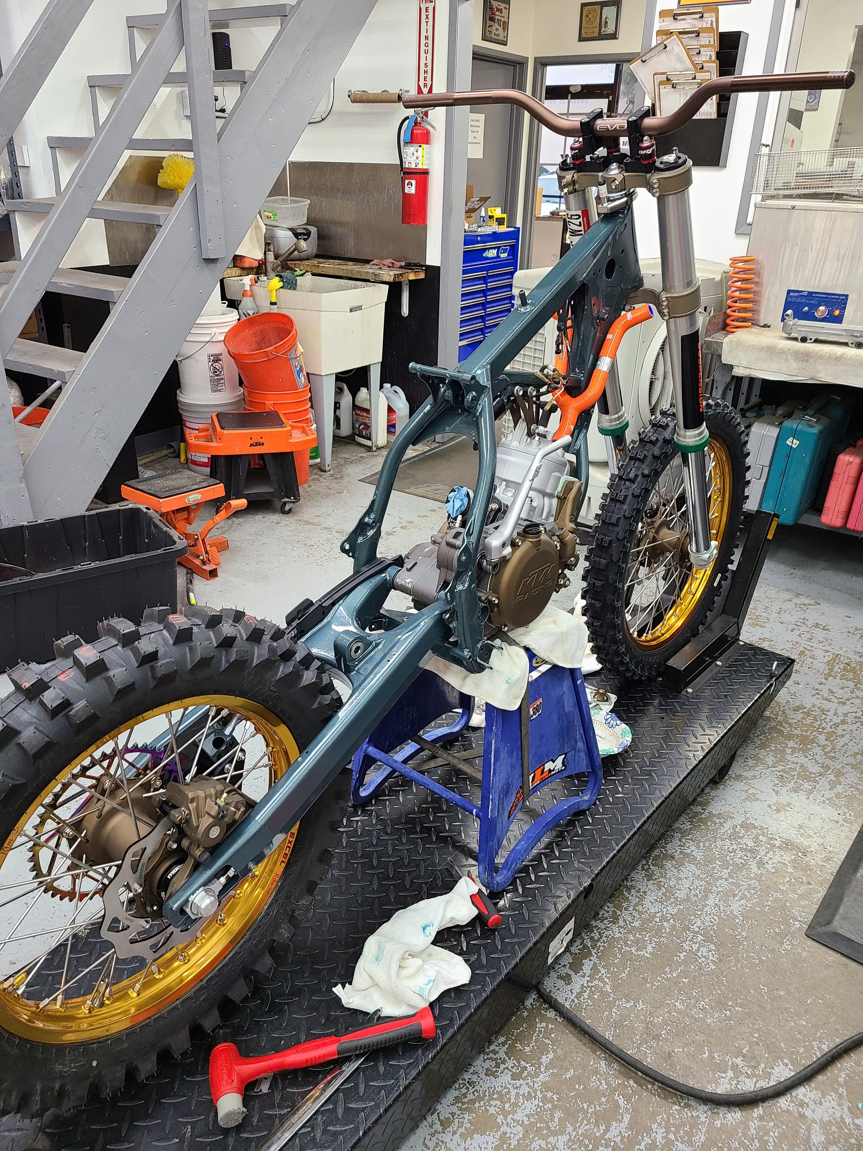 Dirt bike frame and gold wheels mid-rebuild in the ILM service bay